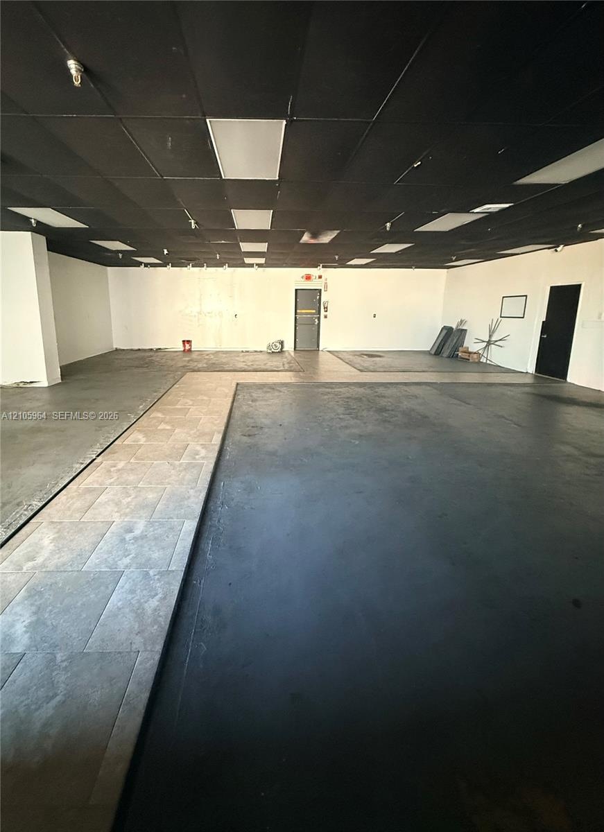 Open interior space featuring a matte black drop ceiling with recessed lighting, smooth white walls, concrete flooring, and tiled floor inlays