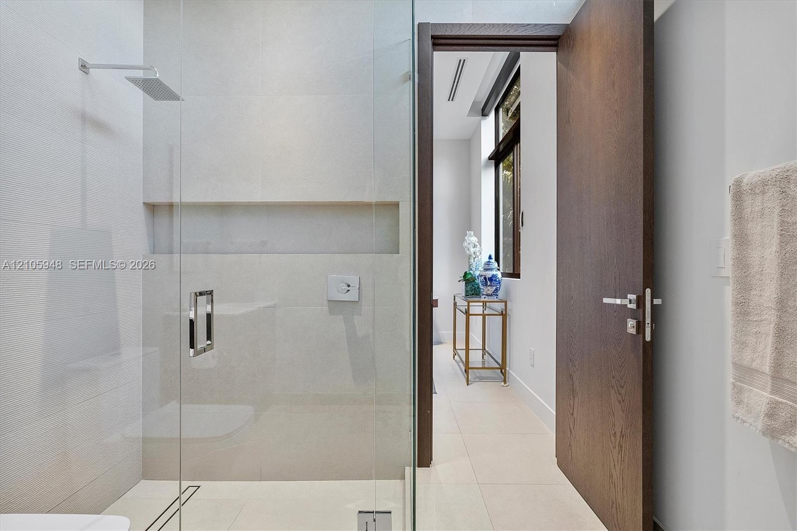 Walk-in shower featuring glass enclosure, wall-mounted rainfall showerhead, and integrated recessed shelving, complemented by a solid wood-finish door