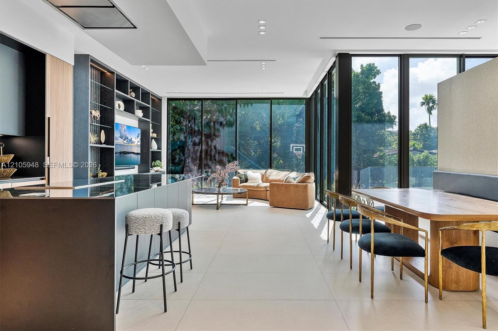 Open-concept interior featuring floor-to-ceiling black-framed windows, built-in floor-to-ceiling shelving, large-format tile flooring, and a kitchen i