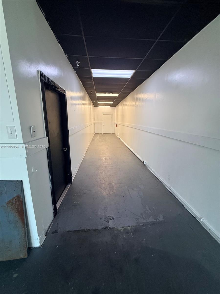 Hallway featuring smooth painted walls, high-contrast dark ceiling panels, recessed fluorescent lighting, and durable gray flooring