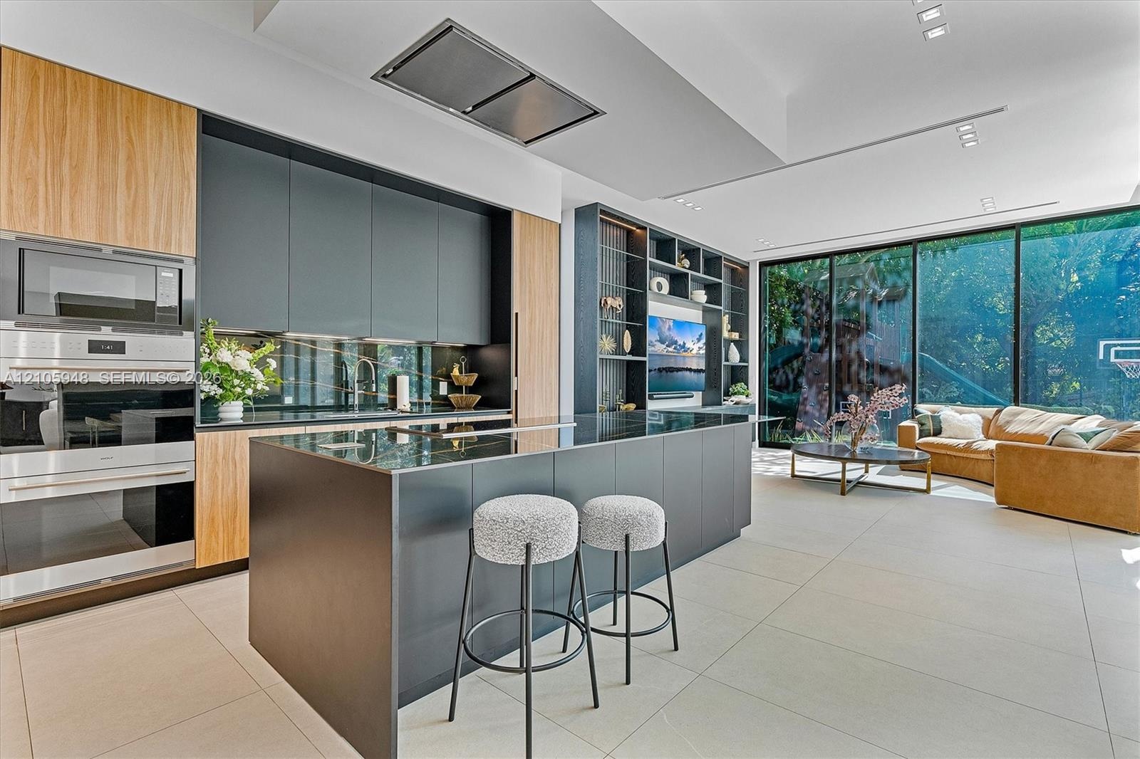 Contemporary kitchen featuring flat-panel cabinetry, a central island with a waterfall edge, stainless steel built-in double wall ovens, ceiling-integ