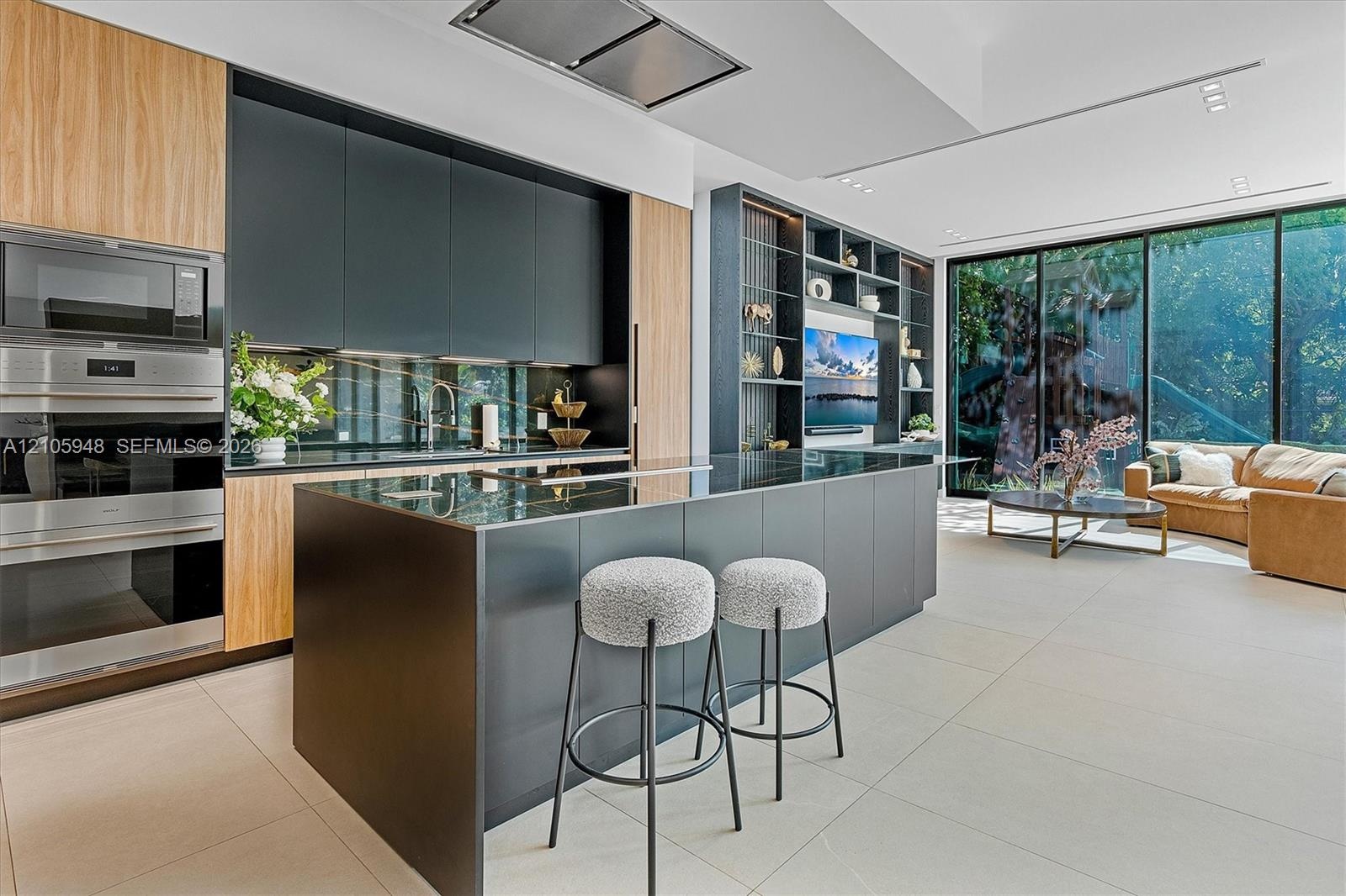 Contemporary kitchen featuring matte cabinetry, wood-finish paneling, a large island with a surface-mounted cooktop, floor-to-ceiling glass sliding do