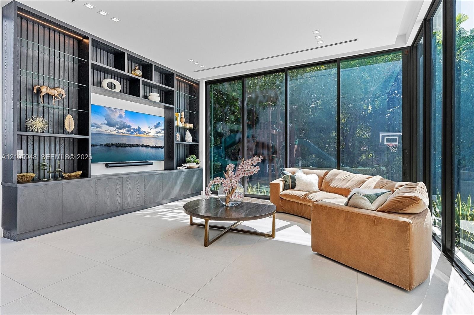 Living space featuring floor-to-ceiling glass walls, built-in custom dark wood cabinetry with integrated glass shelving, recessed lighting, and large-