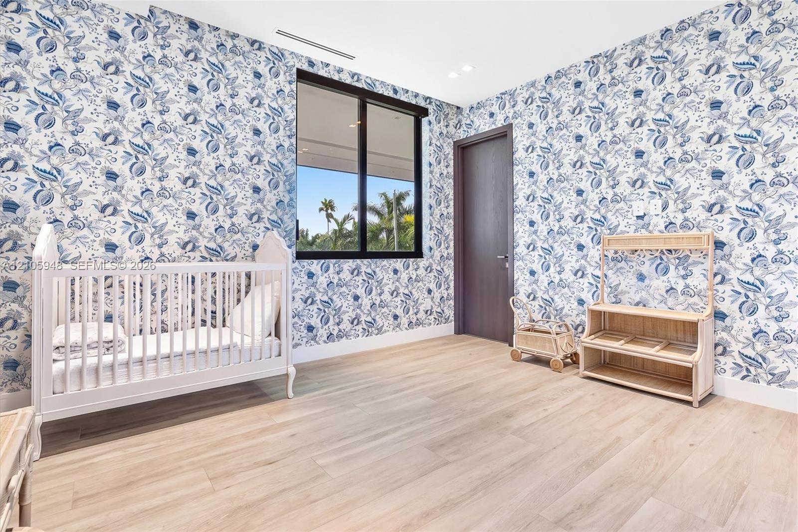Room featuring floral patterned wallpaper, light wood-finish flooring, a black-framed window, and a dark wood-finish interior door with recessed ceili