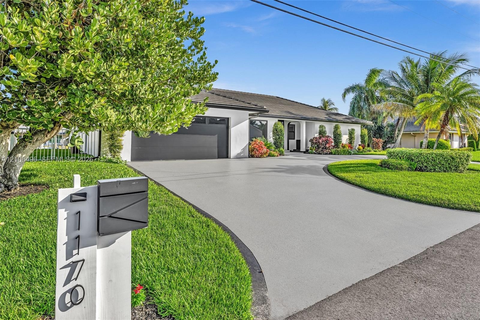 Single-story residence featuring a tile roof, light-toned exterior finish, multi-car garage, expansive concrete driveway, and established landscaping