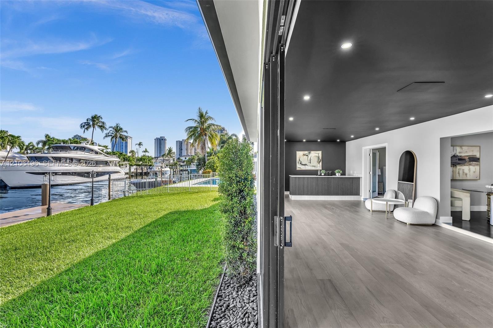 Waterfront property featuring a private boat dock, retractable glass wall system, recessed lighting, wood-finish flooring, and a built-in wet bar