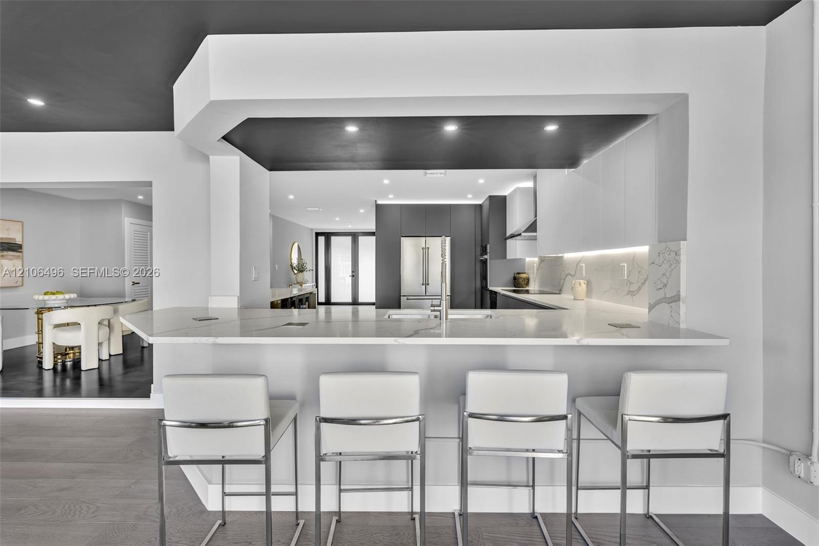 Kitchen featuring a peninsula with a stone-surfaced countertop, integrated under-cabinet lighting, full-height stone backsplash, flat-panel cabinetry,