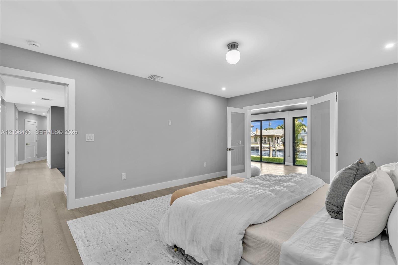 Neutral-toned interior featuring wood-finish flooring, recessed lighting, double glass-panel doors, and sliding glass doors with exterior water exposu