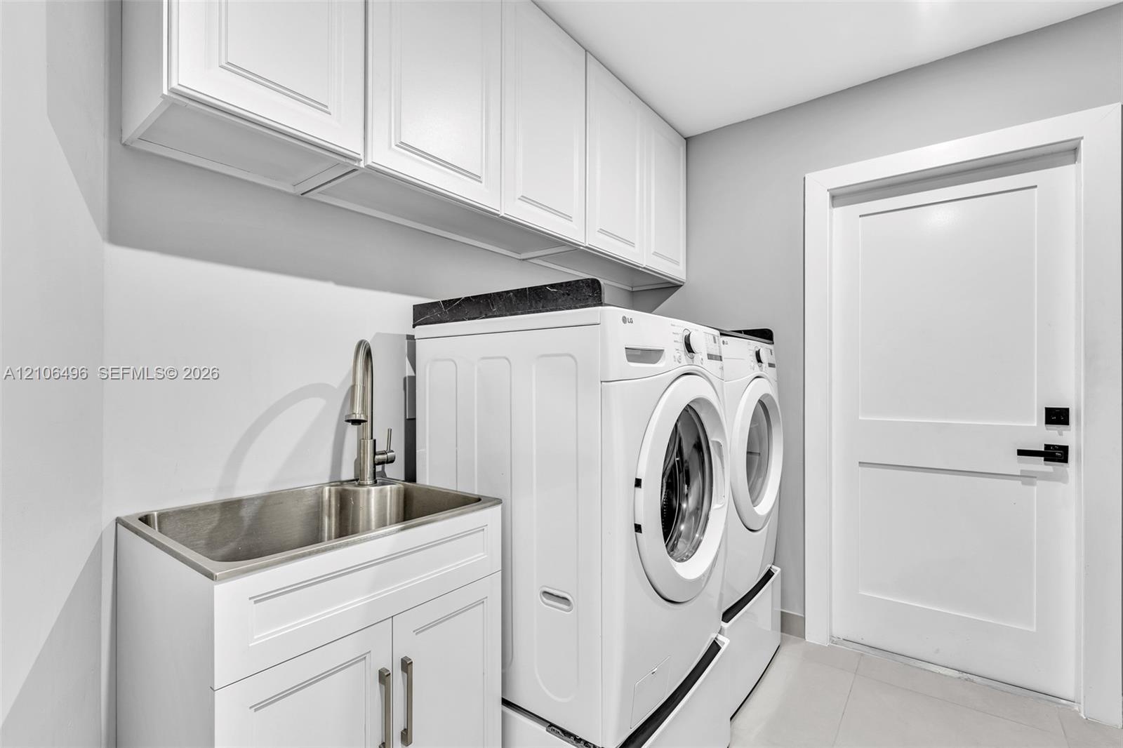 Laundry room featuring white shaker-style upper and lower cabinetry, an integrated stainless steel utility sink with a high-arch pull-down faucet, dar