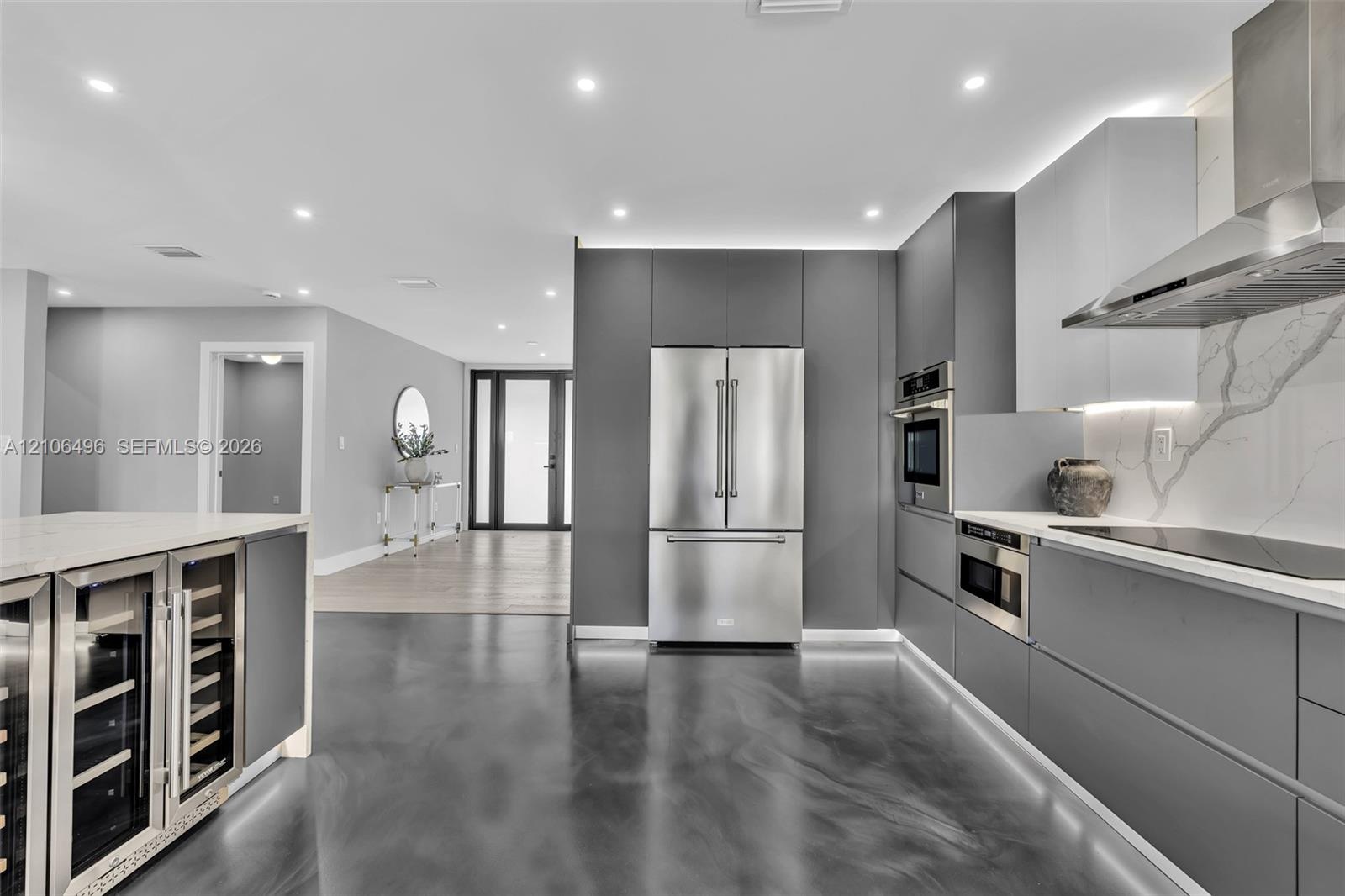 Modern kitchen featuring handleless cabinetry, stainless steel appliances, a built-in wine refrigerator, under-cabinet lighting, and a stone-patterned