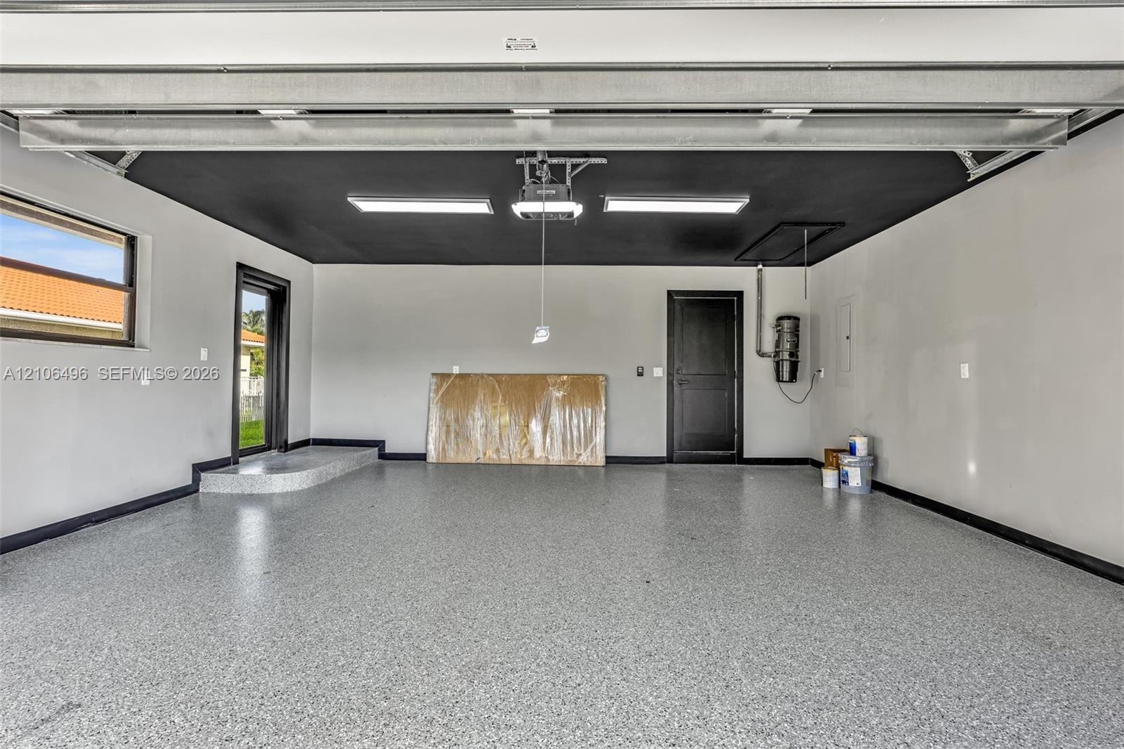 Garage featuring a speckled epoxy floor coating, contrasting black ceiling, dual flush-mount LED lighting, and an elevated entryway threshold