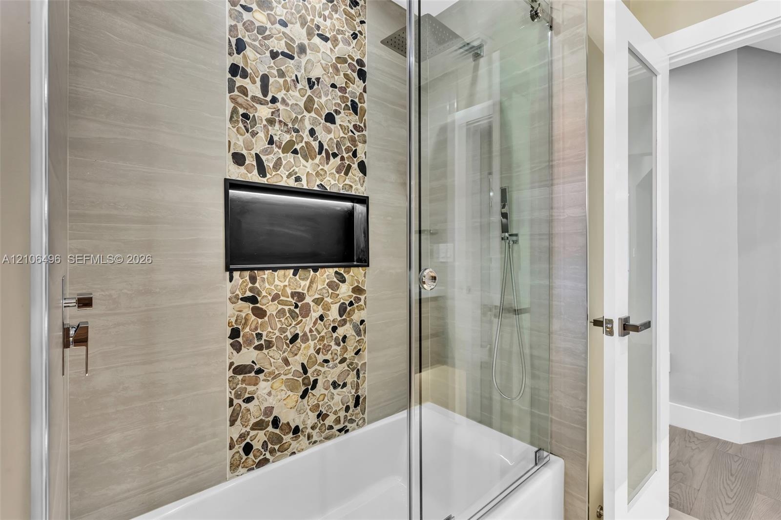 Shower and tub combination featuring horizontal tile surrounds, a decorative vertical pebble-tile inlay, integrated black-framed shower niche, glass s