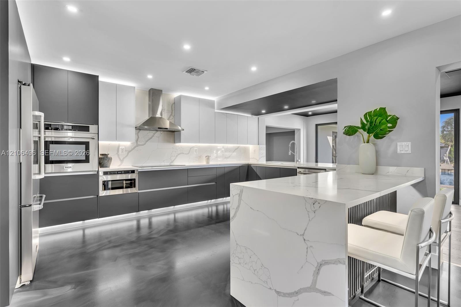 Kitchen featuring two-tone flat-panel cabinetry, a waterfall-edge stone countertop, integrated stainless steel appliances, and under-cabinet accent li