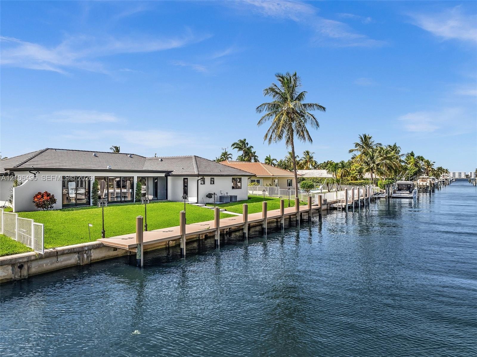 Waterfront residence featuring a private dock, expansive grass lawn, concrete seawall, and glass sliding exterior doors