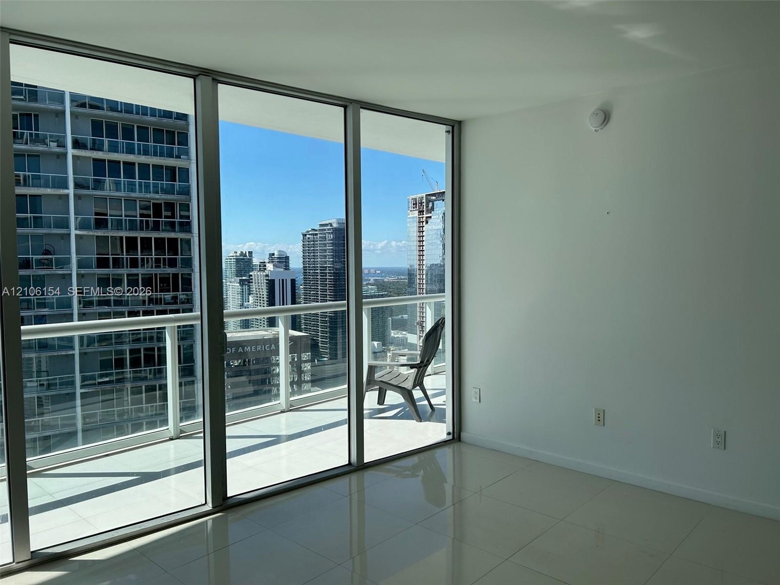 Floor-to-ceiling glass walls, polished tile flooring, and a private balcony with metal railings and a glass surround