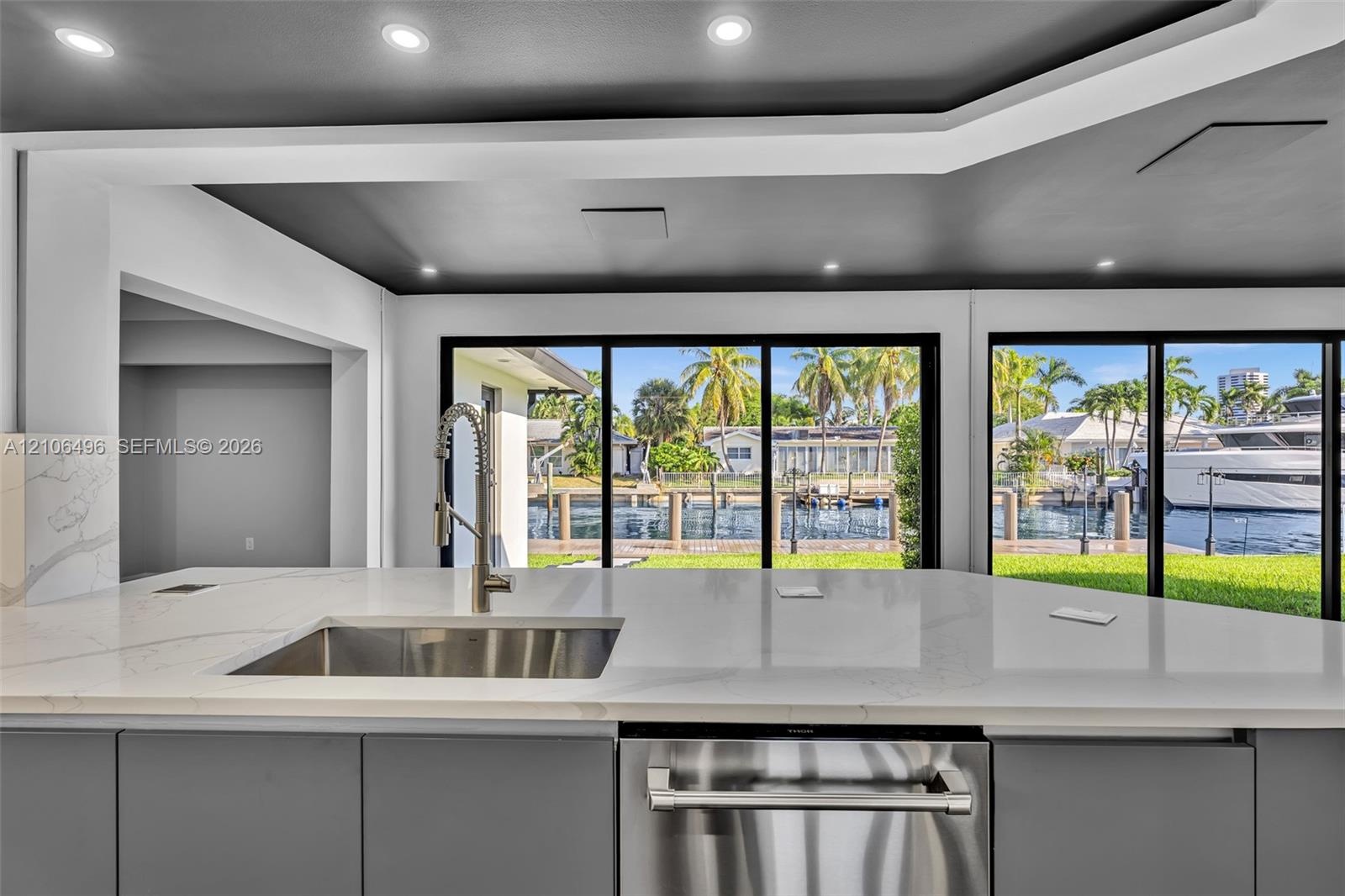 Kitchen featuring a stone-surface island, undermount stainless steel sink with a high-arc faucet, integrated stainless steel dishwasher, flat-panel ca