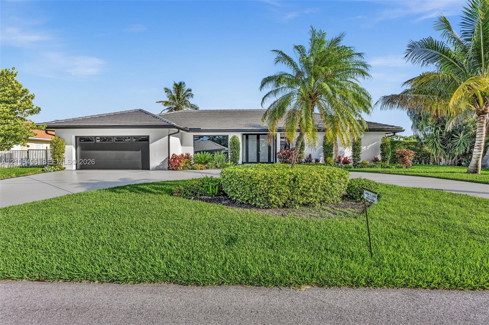 Single-story residence featuring a smooth stucco facade, hip roof with dark tiles, attached two-car garage, and manicured landscaping with established