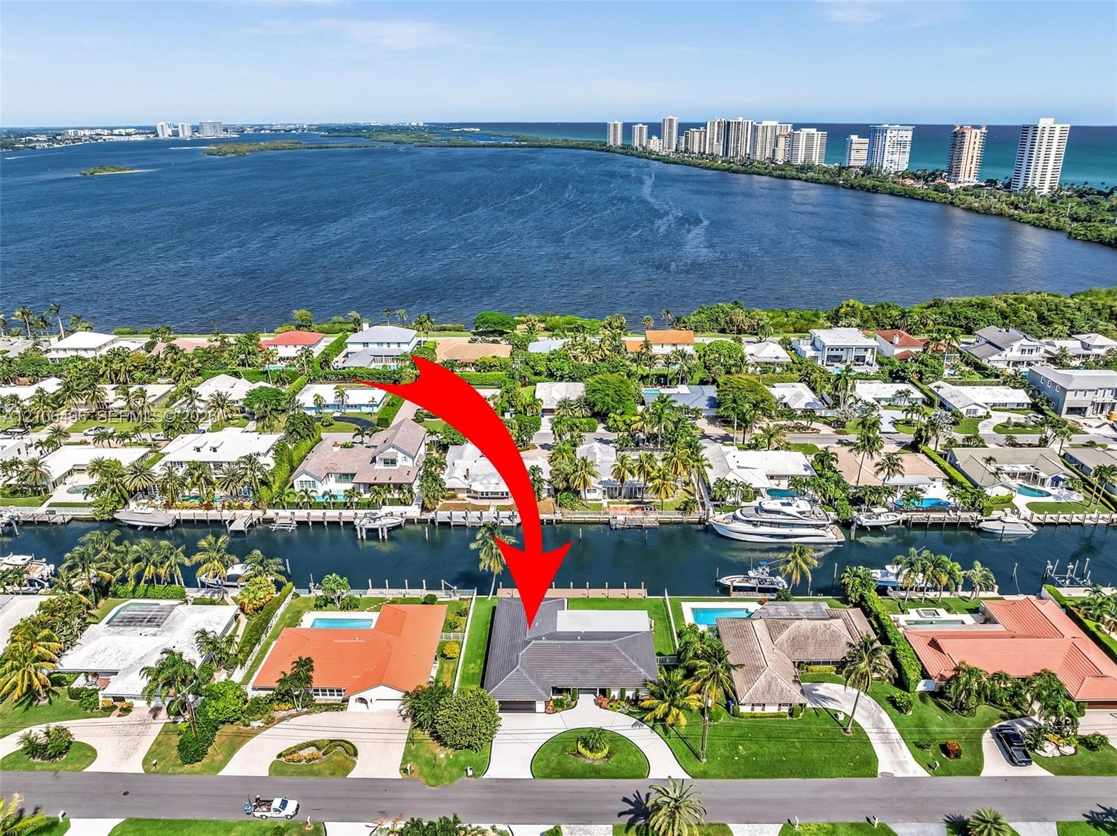 Aerial perspective of a canalfront property featuring a private boat dock, multi-pitched roofline, curved paved driveway, and mature landscaping