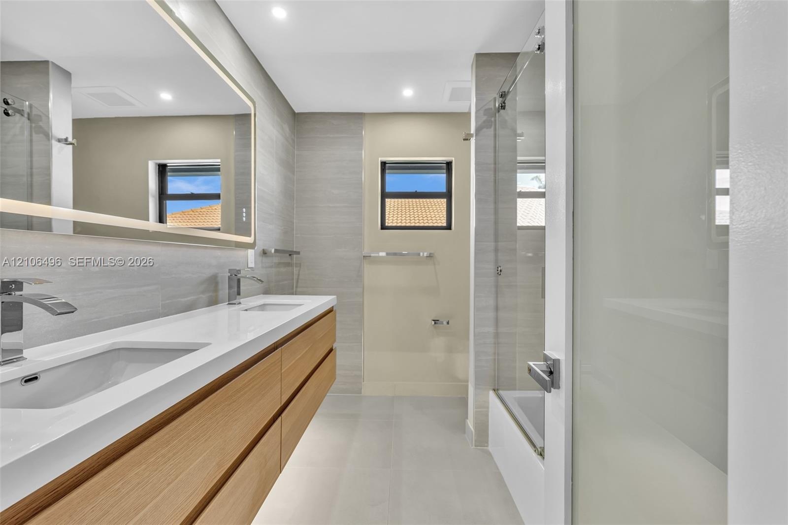 Floating double vanity with a stone countertop and dual undermount sinks, illuminated mirror, wood-finish cabinetry, and a glass-enclosed shower featu