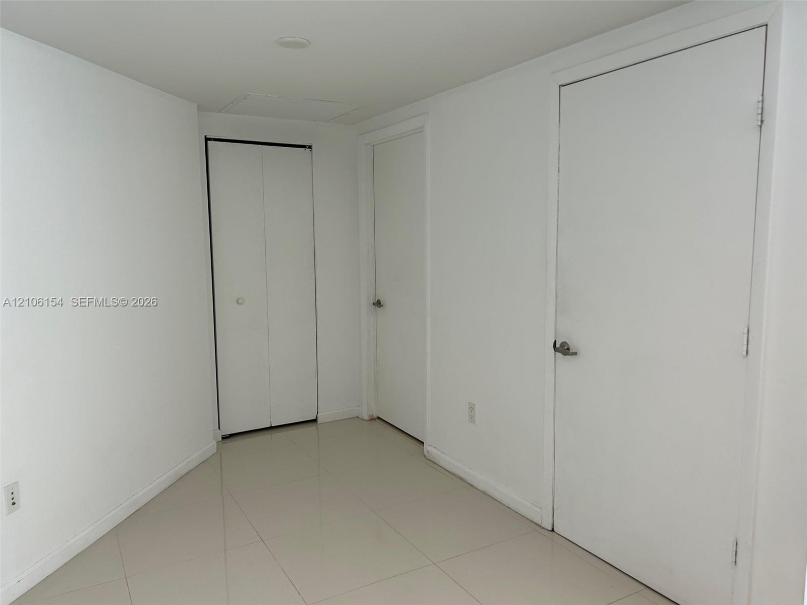 Interior space featuring neutral wall tones, large-format tile flooring, a dual-panel bi-fold closet, and two solid-core doors with brushed-metal hard