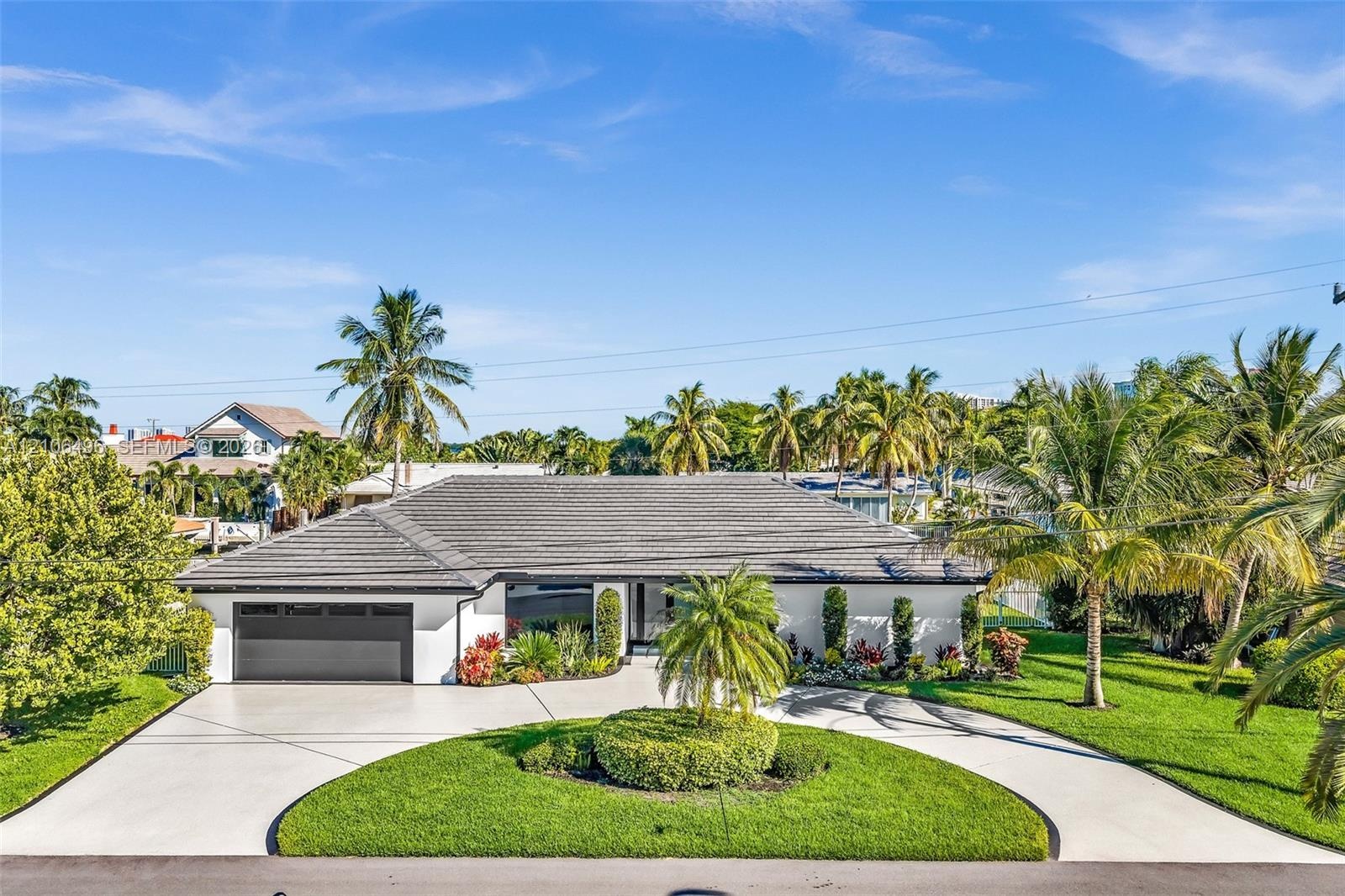 Single-story residence featuring a low-pitched tiled roof, a circular concrete driveway, and an attached two-car garage, complemented by mature tropic