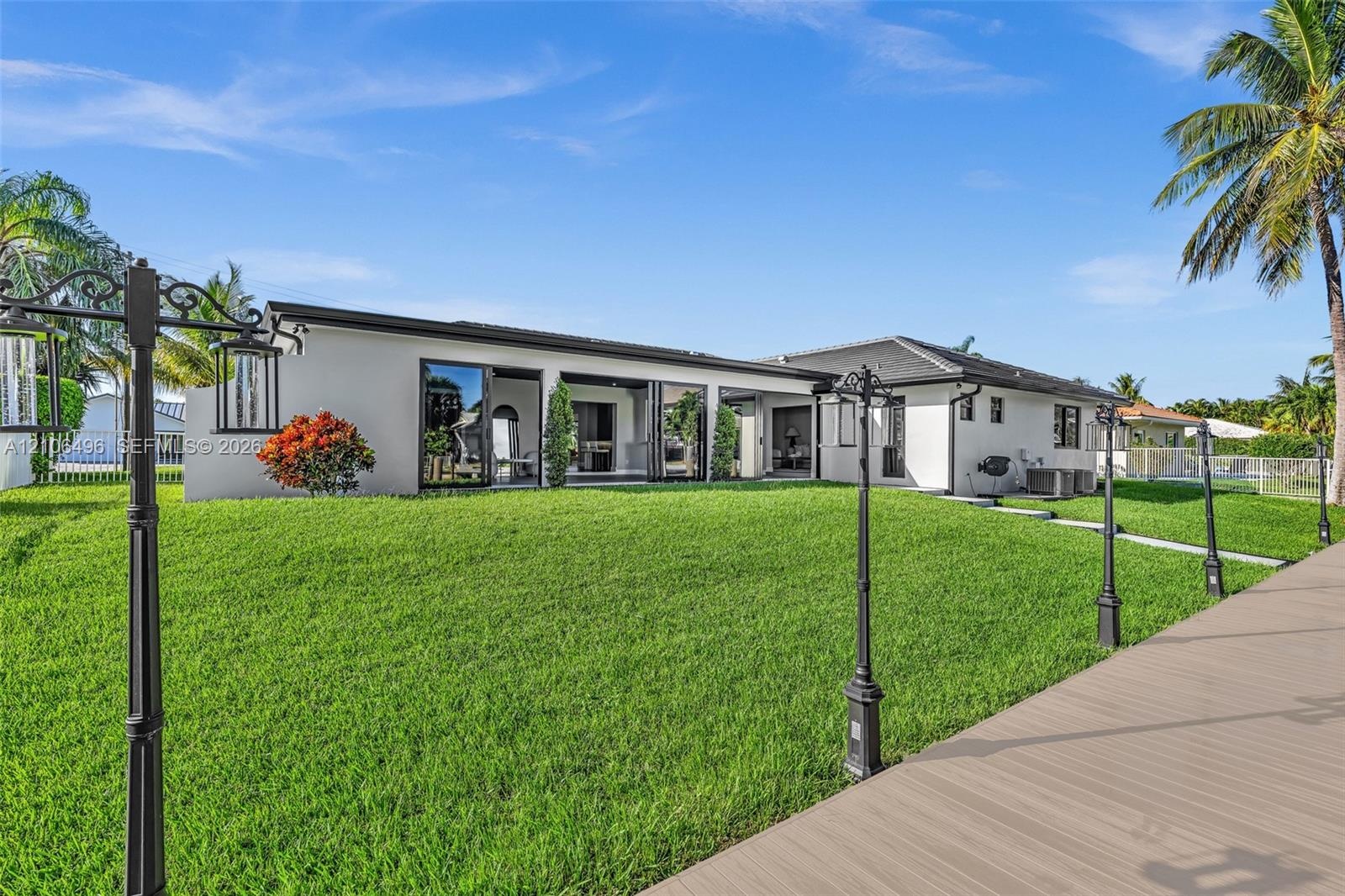 Exterior of a single-story residence featuring a smooth stucco facade, multi-panel sliding glass doors, a wide composite deck, and custom post-mounted