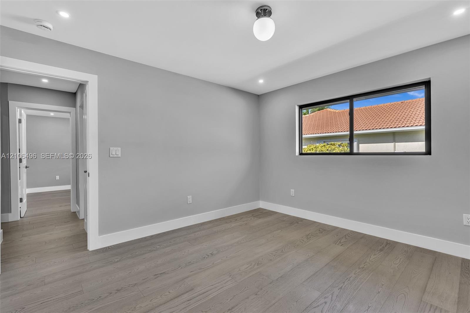 Interior space featuring wood-finish flooring, neutral wall paint, recessed lighting, a globe-style light fixture, and a black-framed window