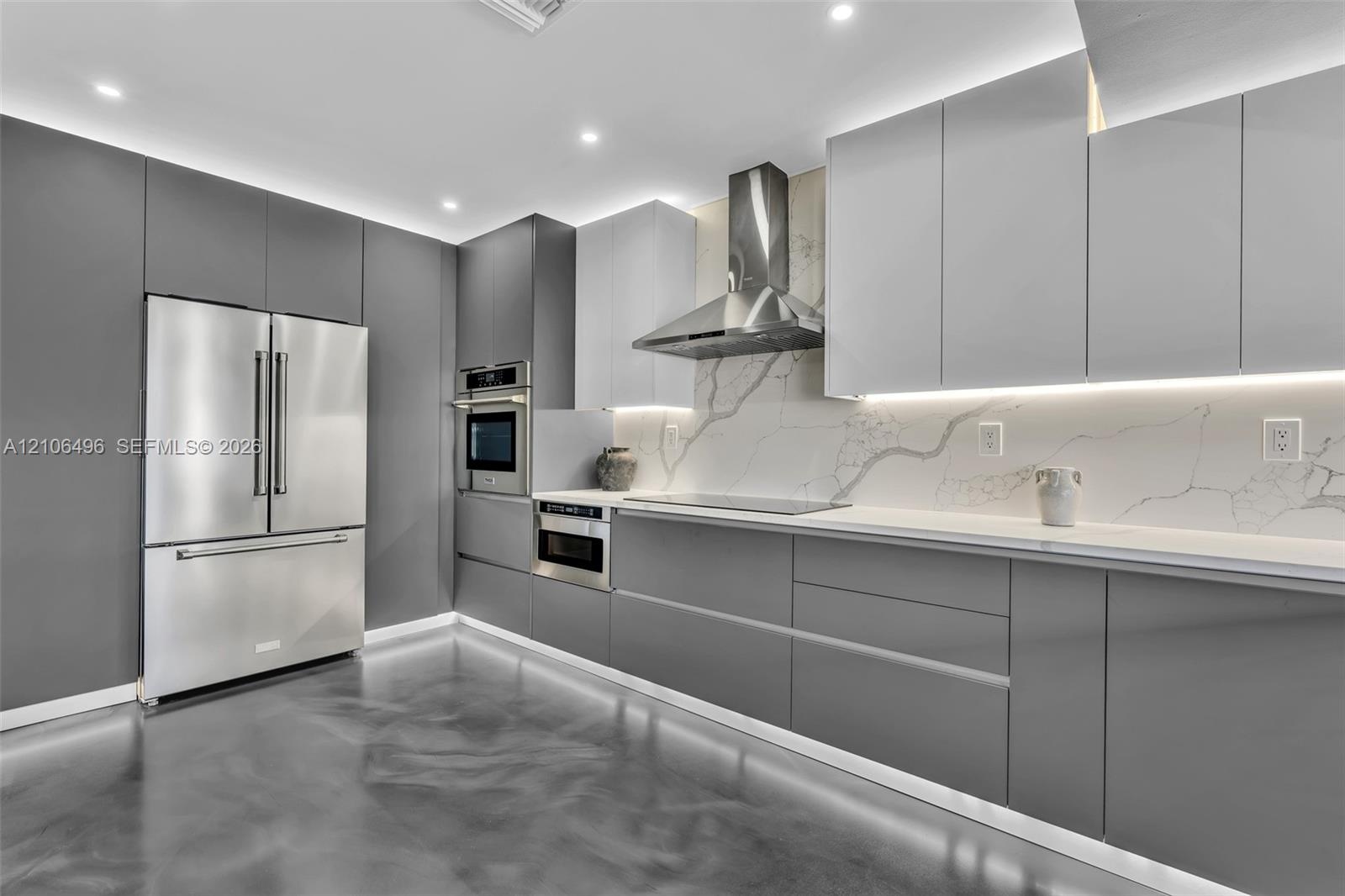 Kitchen featuring floor-to-ceiling cabinetry, stainless steel appliances, stone-surface backsplash, integrated under-cabinet lighting, and polished co