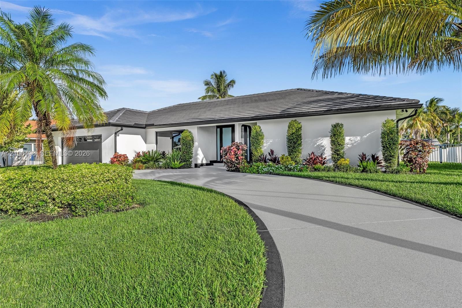 Single-story residence featuring a low-pitched tiled roof, smooth stucco exterior, circular concrete driveway with decorative border, and established 