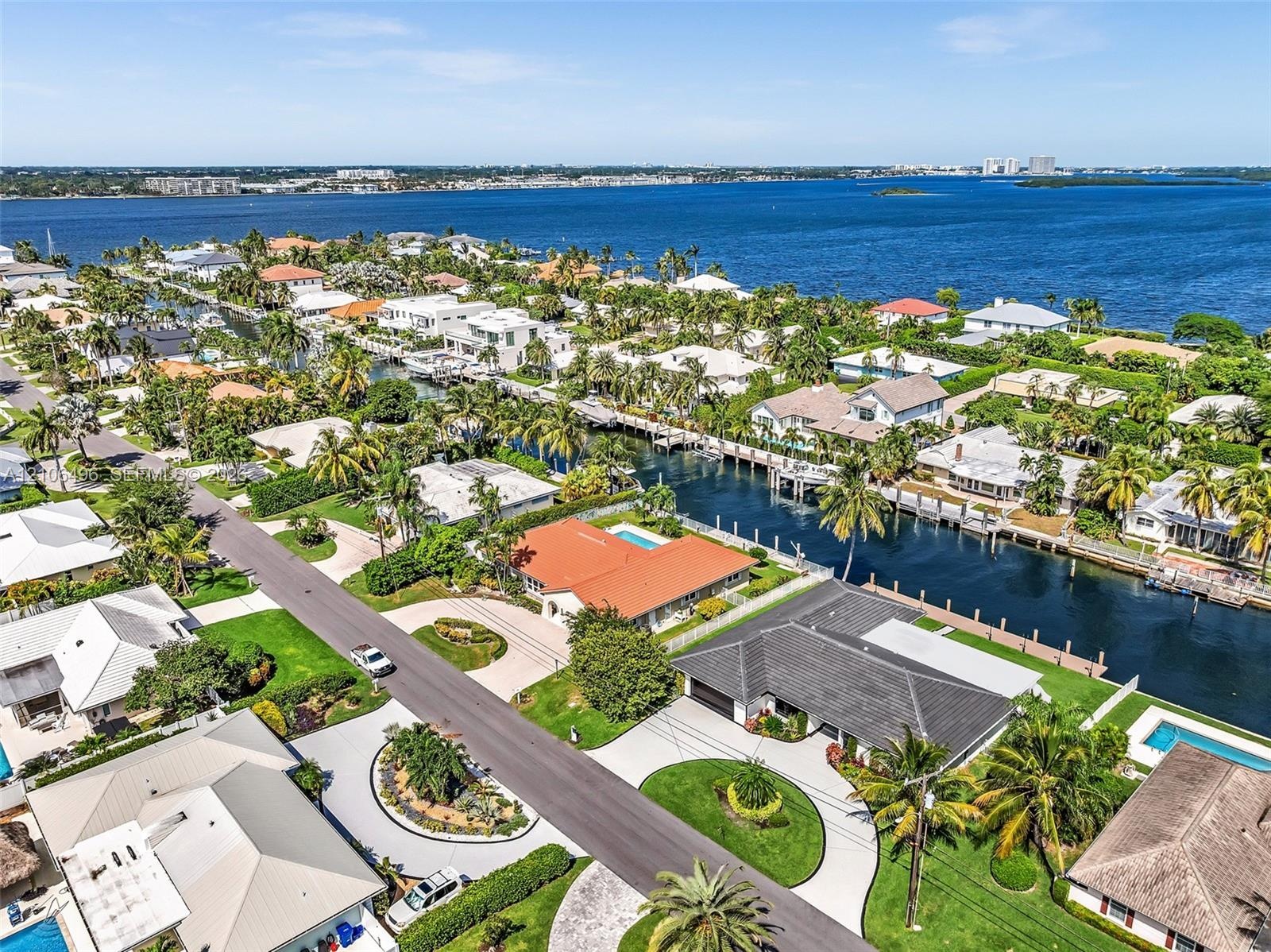 Aerial perspective of a waterfront property featuring a tile roof, paved circular driveway, landscaped lawn, and a private swimming pool