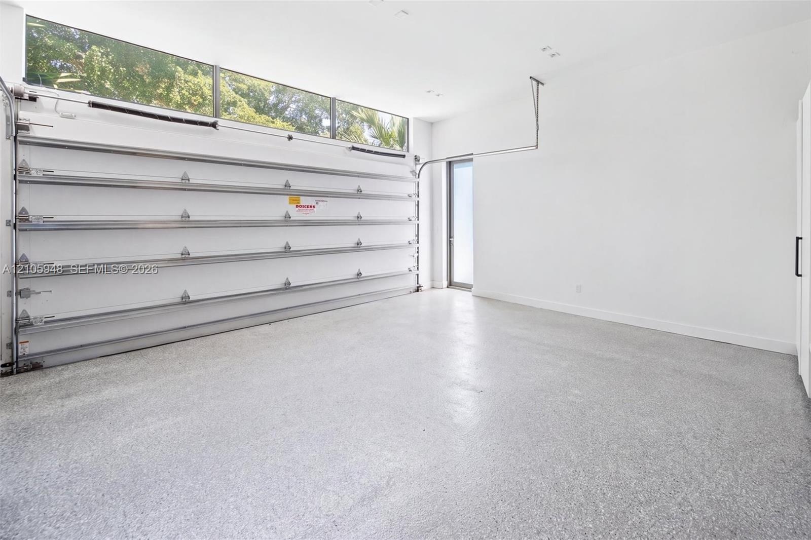 Garage space featuring speckled epoxy flooring, white paneled walls, a ceiling-mounted automatic door opener, and a row of horizontal transom windows