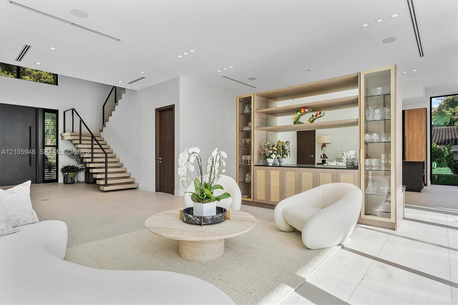 Open floor plan featuring a floating staircase with metal railings, built-in floor-to-ceiling cabinetry with glass display shelving, recessed ceiling 