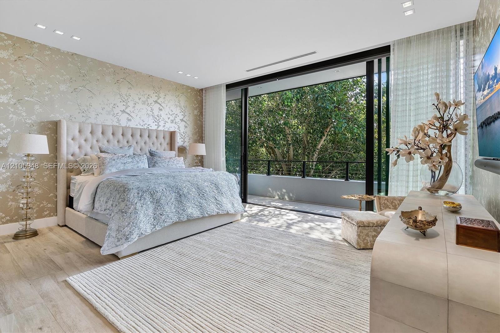 Floor-to-ceiling sliding glass doors opening to a balcony, light-toned wood-finish flooring, recessed ceiling lighting, and patterned wallpaper featur