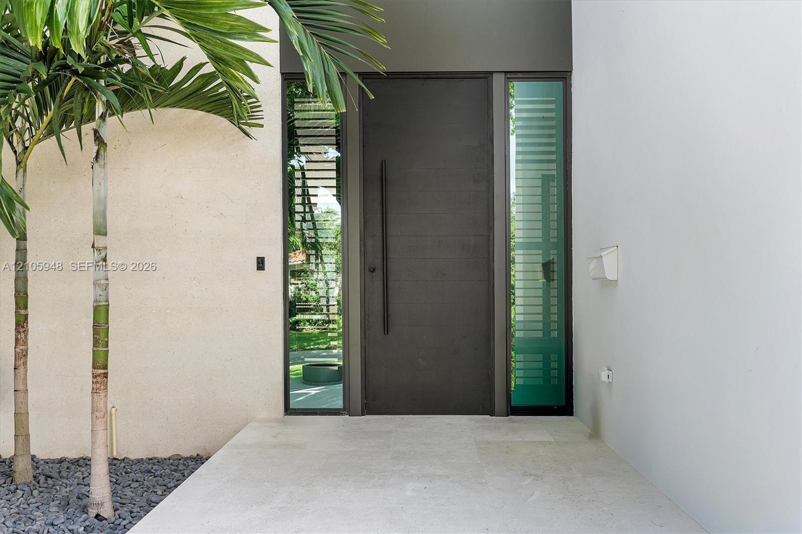 Entry featuring a dark horizontal-plank door with an elongated vertical handle, framed by full-height frosted glass sidelights on a neutral-toned ston