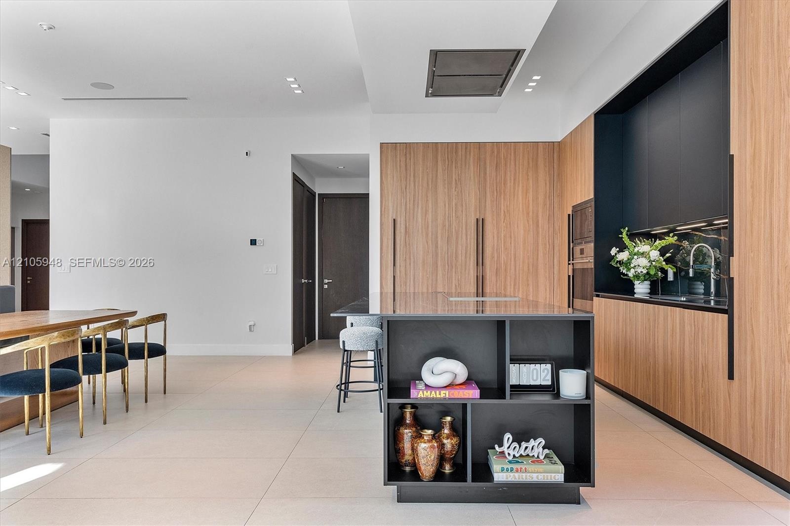 Modern kitchen featuring wood-finish cabinetry, matte black integrated shelving, a central island with storage, built-in wall appliances, and tile flo