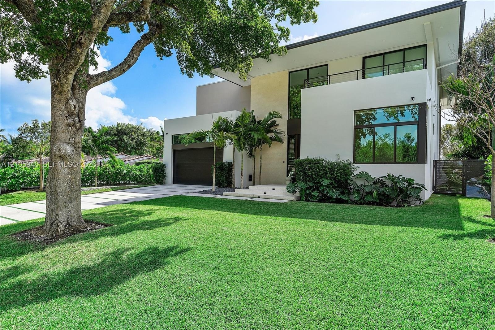 Modern two-story architectural exterior featuring smooth stucco siding, large-pane windows, a second-level balcony with metal railing, and a paved mul