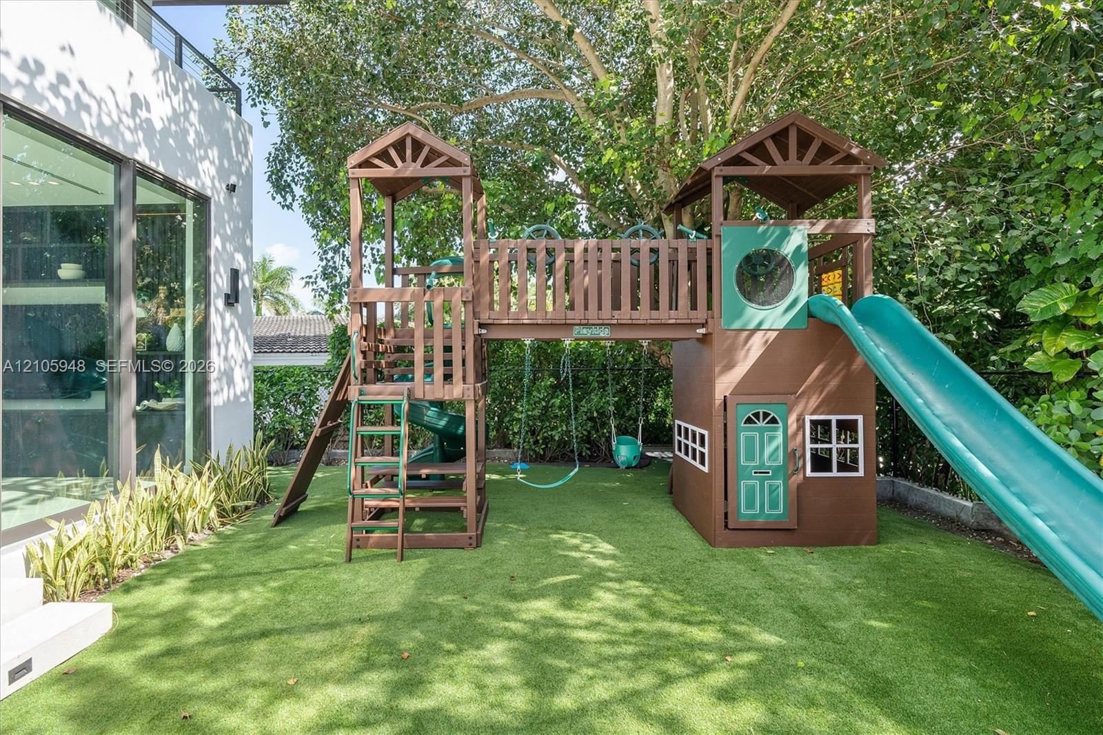 Outdoor area featuring low-maintenance synthetic turf, integrated wood play structure with dual towers and slide, and established perimeter privacy he