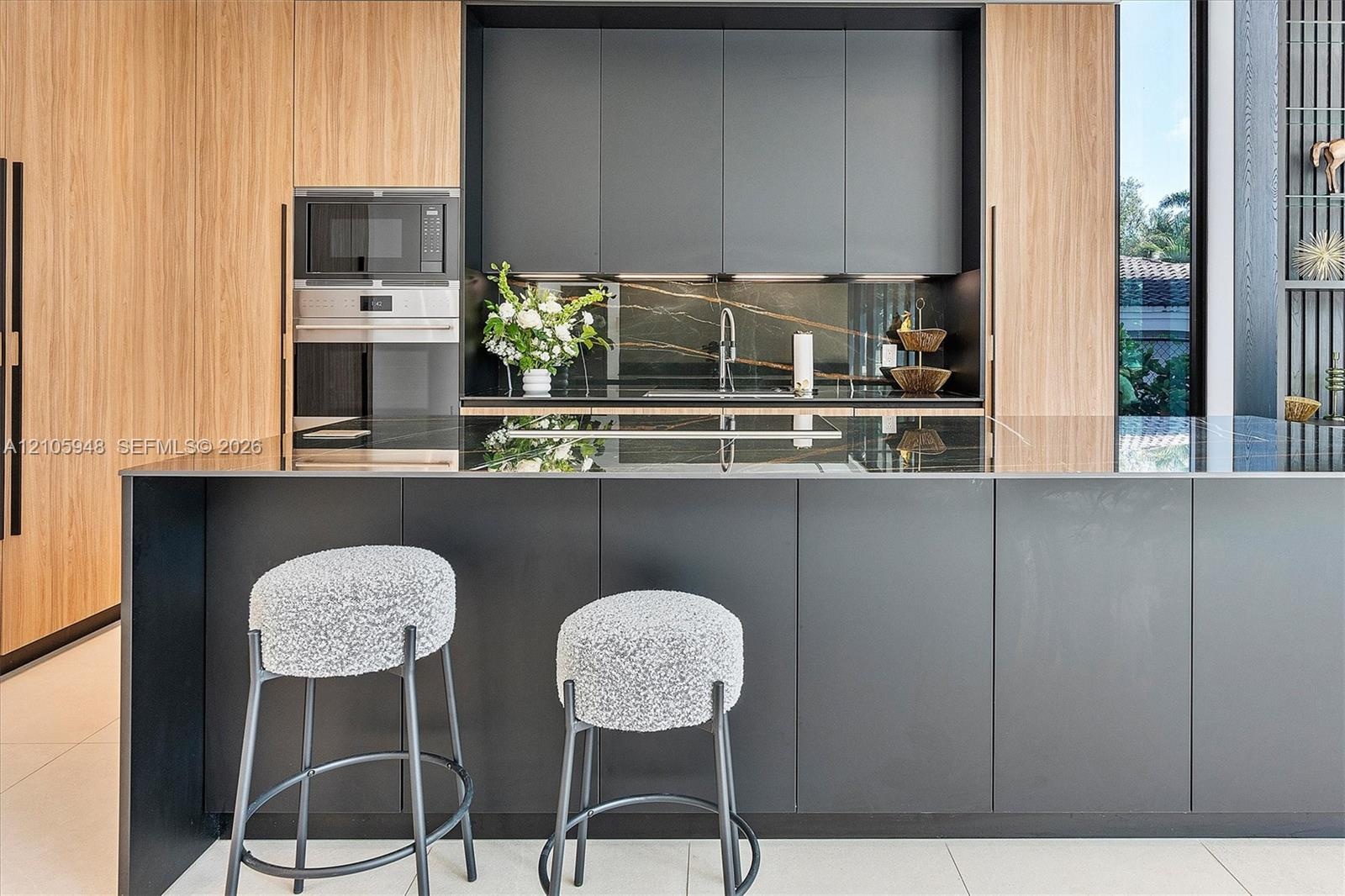 Modern kitchen featuring matte charcoal cabinetry, wood-finish paneling, an expansive island with a stone surface, built-in stainless steel appliances