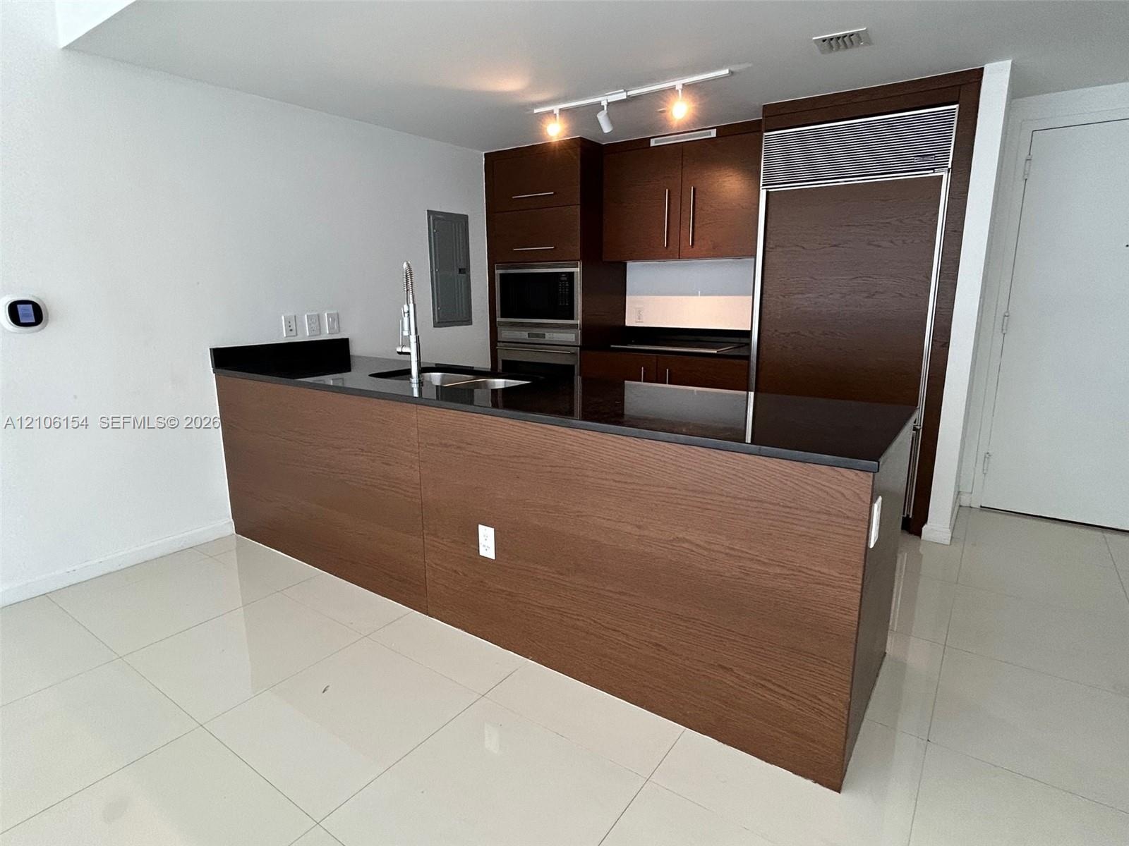 Kitchen featuring dark wood-finish cabinetry, black stone countertops, integrated stainless steel refrigerator, stainless steel built-in microwave and