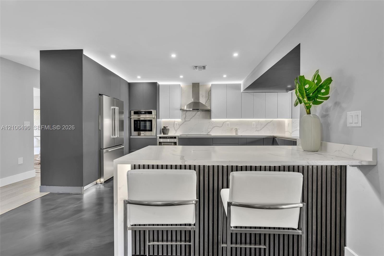 Modern kitchen featuring dual-tone cabinetry, quartz countertops, stainless steel appliances, an island with slatted detailing, and under-cabinet ligh