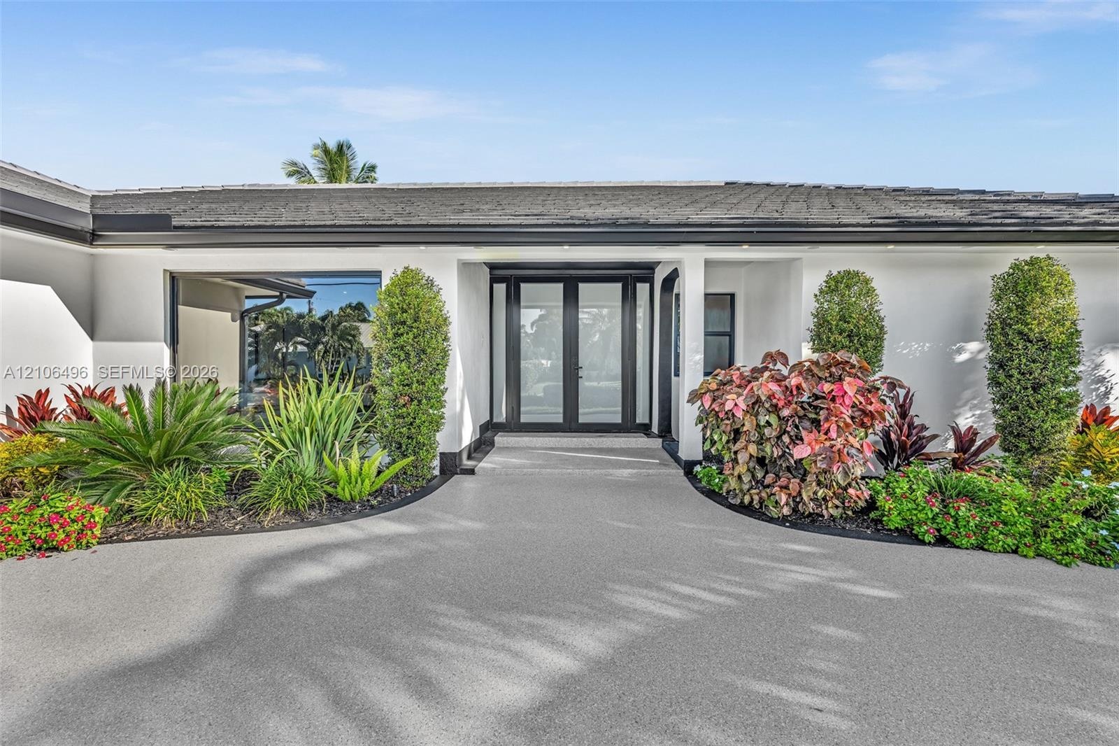 Contemporary exterior featuring a textured concrete driveway, dual glass entry doors with dark frames, and manicured landscaping