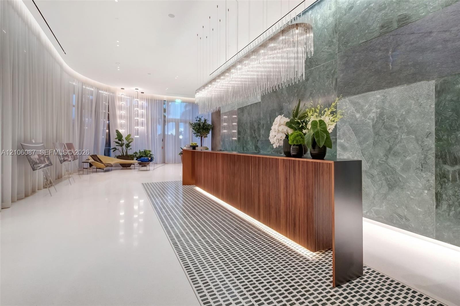 Reception area featuring a wood-panel console, large-format green stone wall cladding, custom crystal-style pendant lighting, polished white flooring,