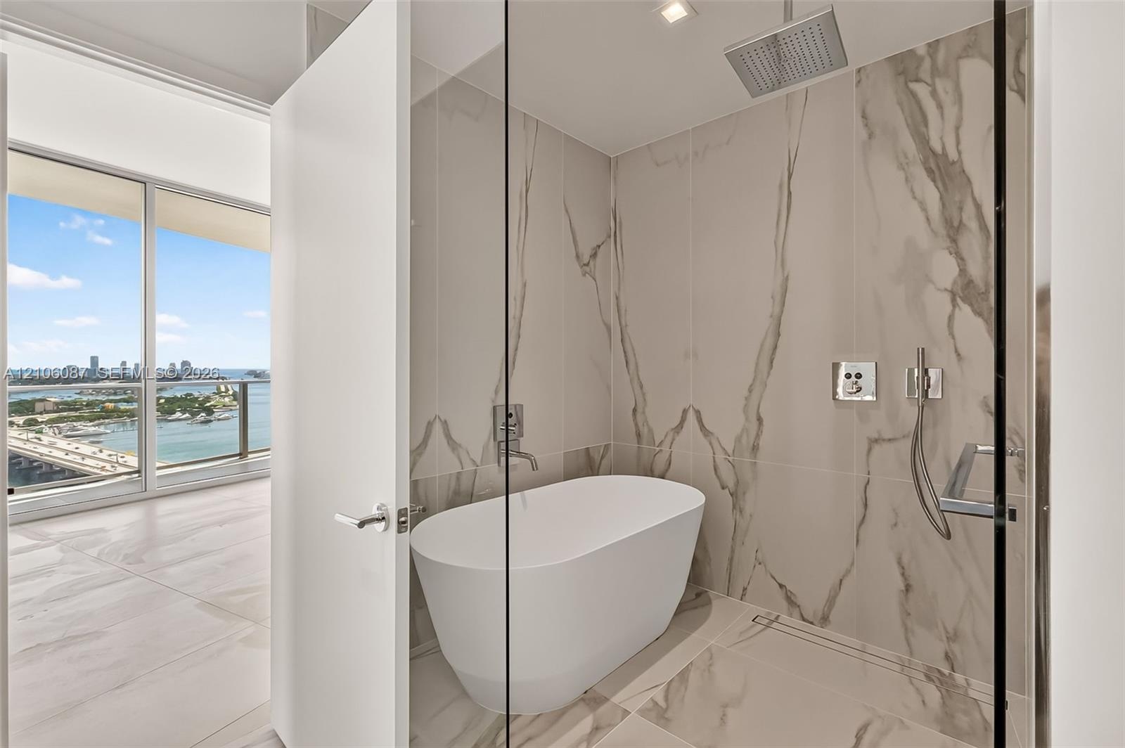 Freestanding soaking tub, floor-to-ceiling large-format tile wall surround, rain-style shower head with handheld attachment, glass-enclosed wet room, 