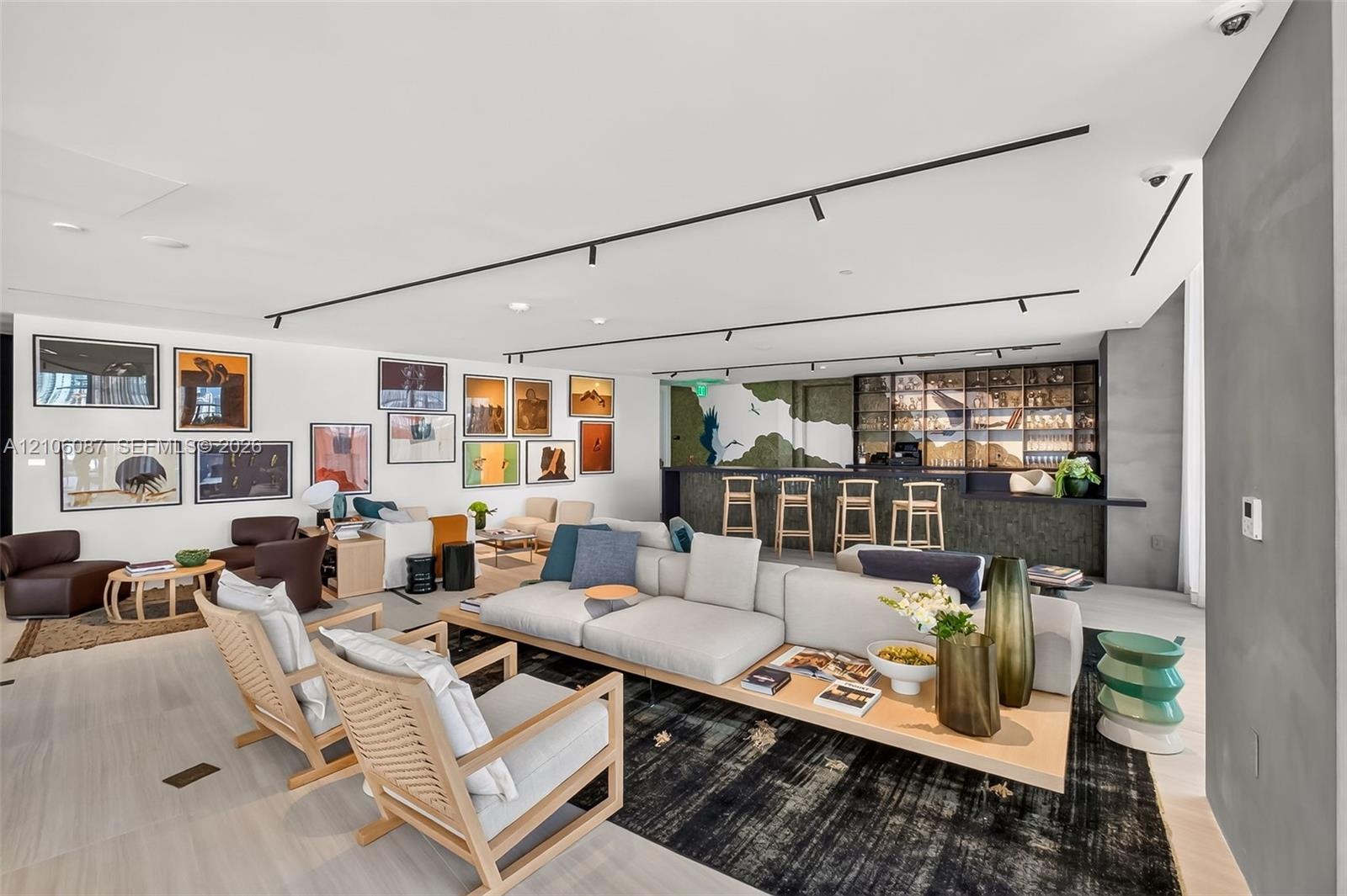 Open-concept space featuring light-toned wood-finish flooring, recessed track lighting, a built-in wet bar with dark stone-finish facing, and decorati