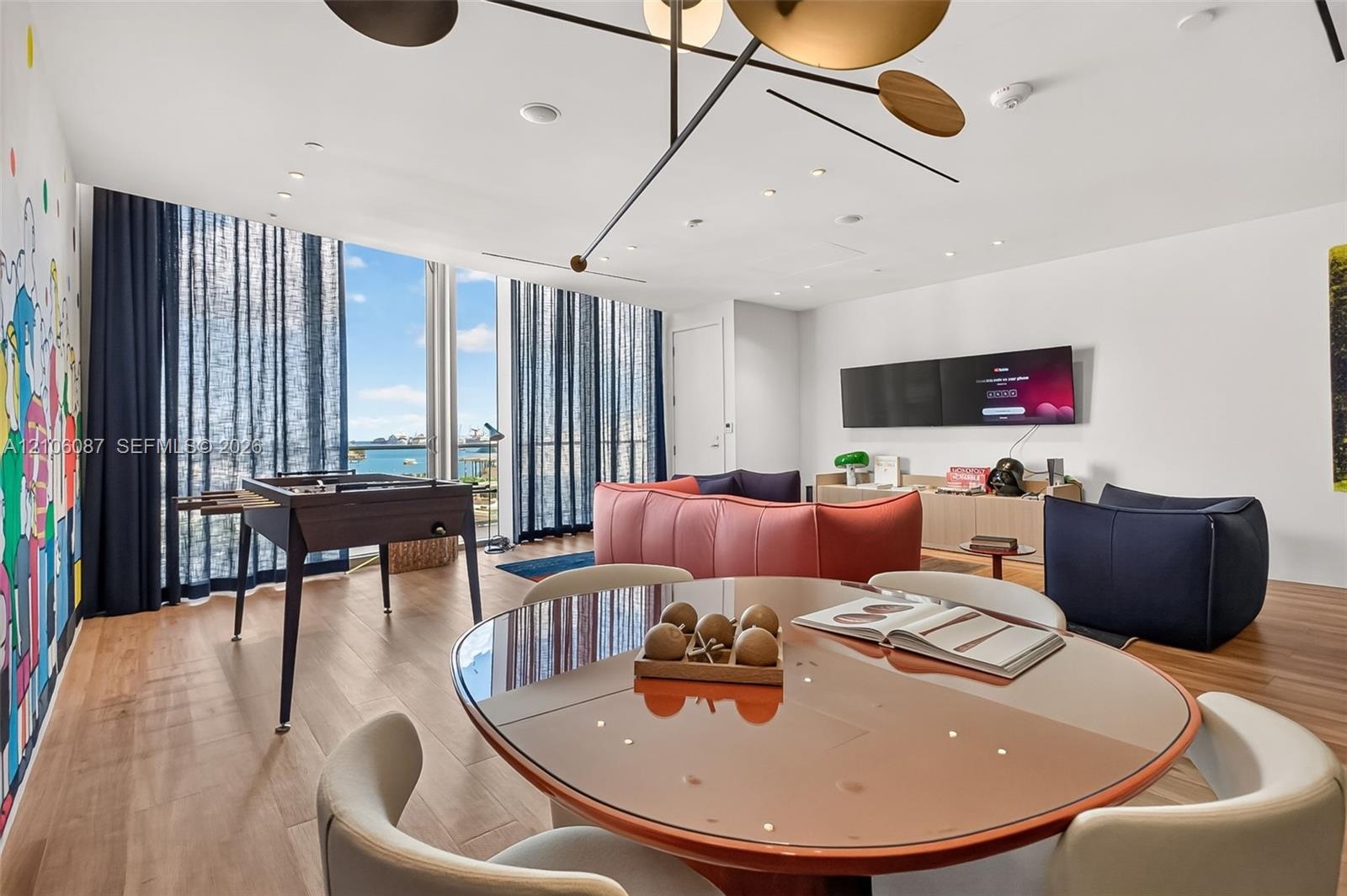 Living area featuring floor-to-ceiling windows, wood-finish flooring, custom geometric overhead lighting, and built-in wall-mounted cabinetry