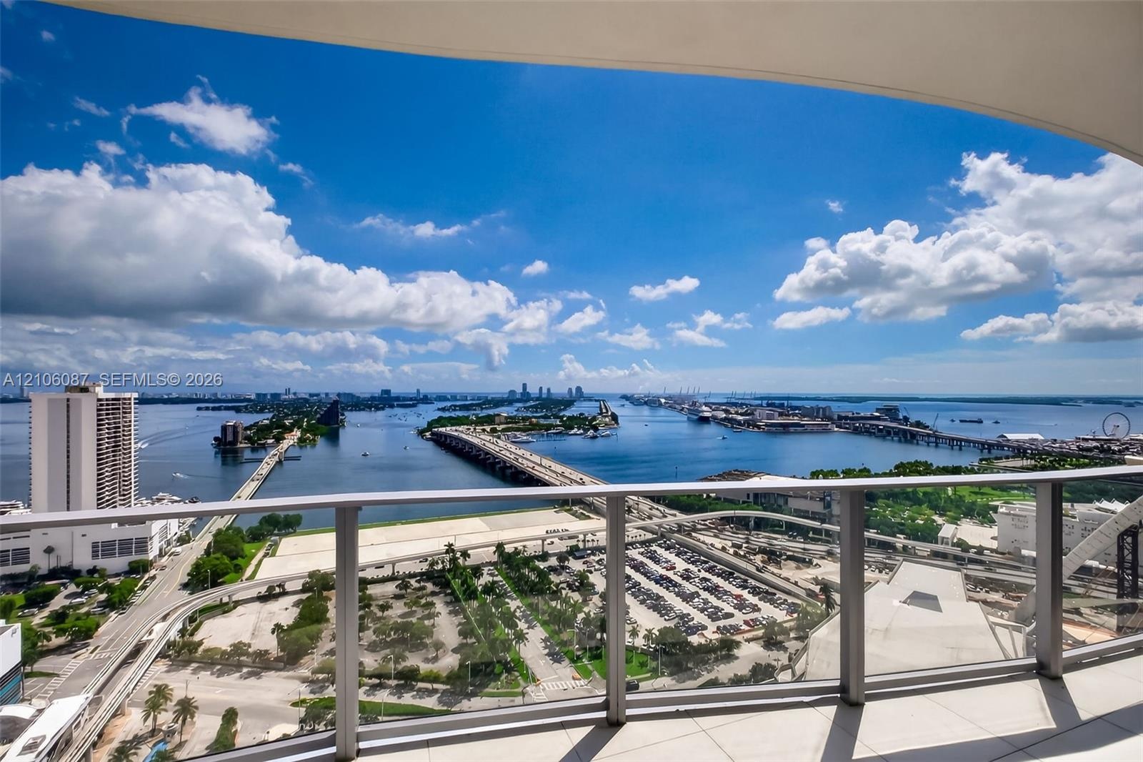 Private balcony featuring glass panel railing and tile flooring, showcasing panoramic water, bridge, and cityscape scenery