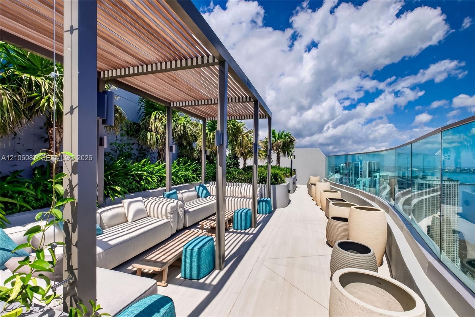 Rooftop terrace featuring a slatted metal pergola, light-toned tile flooring, glass panel perimeter railing, and integrated landscaping
