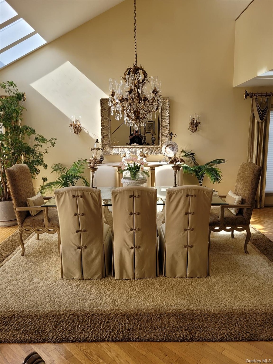 Vaulted ceiling with skylights, chandelier lighting, sconce lighting, mirror with ornate frame, and wood-finish flooring