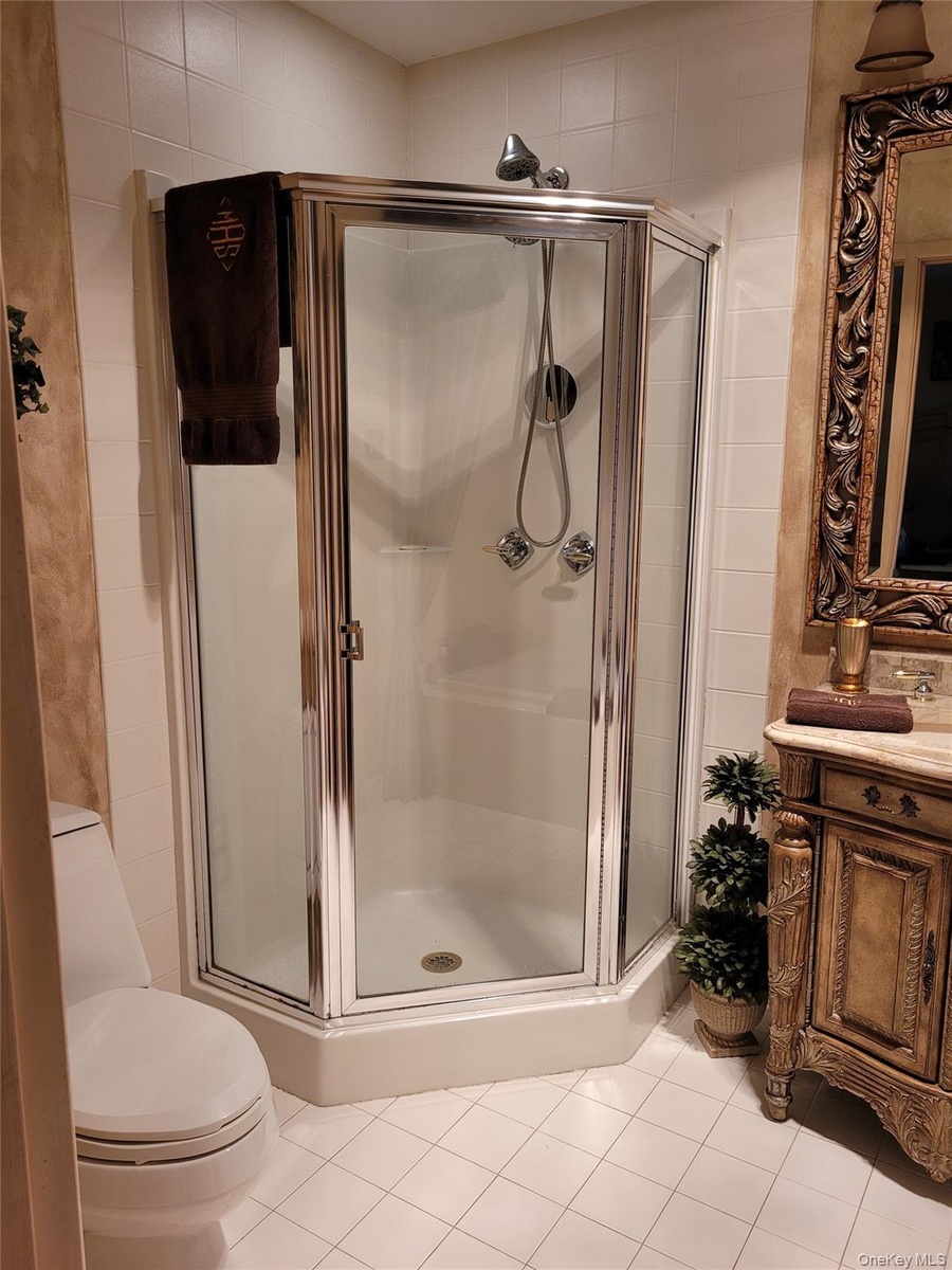 Tiled flooring with a corner shower enclosure featuring a glass door and chrome trim