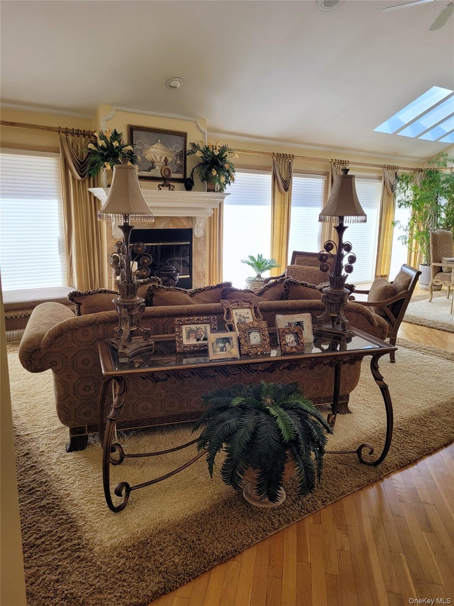 Hardwood flooring, fireplace with ornate mantel, multiple windows with custom window treatments, and a skylight ceiling feature